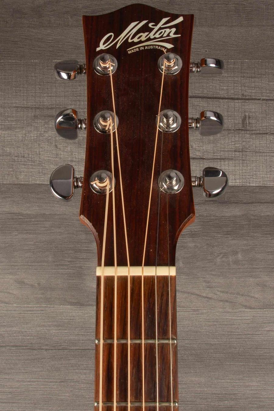 Close-up of Maton M808 guitar headstock showcasing tuning pegs and logo on natural wood background.