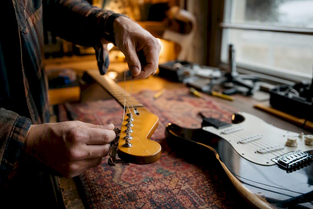 Hands winding new strings on acoustic guitar tuning peg