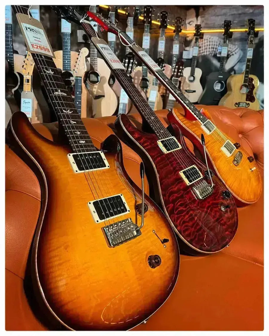 Three PRS guitars displayed on a couch, highlighting PRS guitars popularity reasons in the music world.