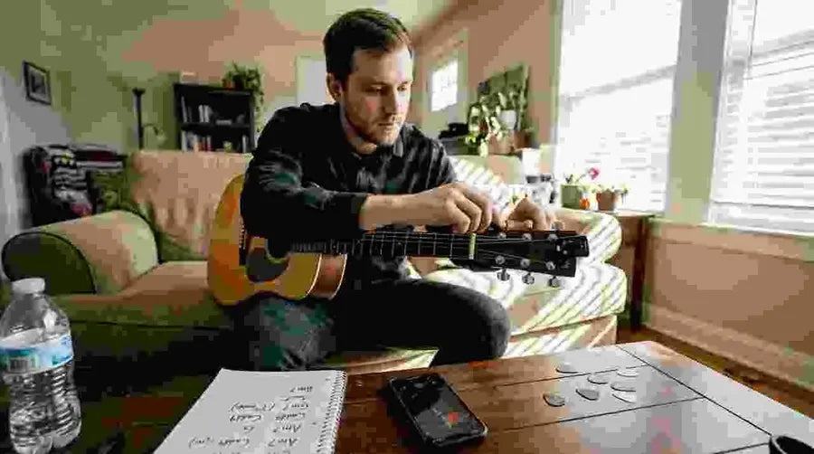 Guitarist tuning acoustic guitar with tuner