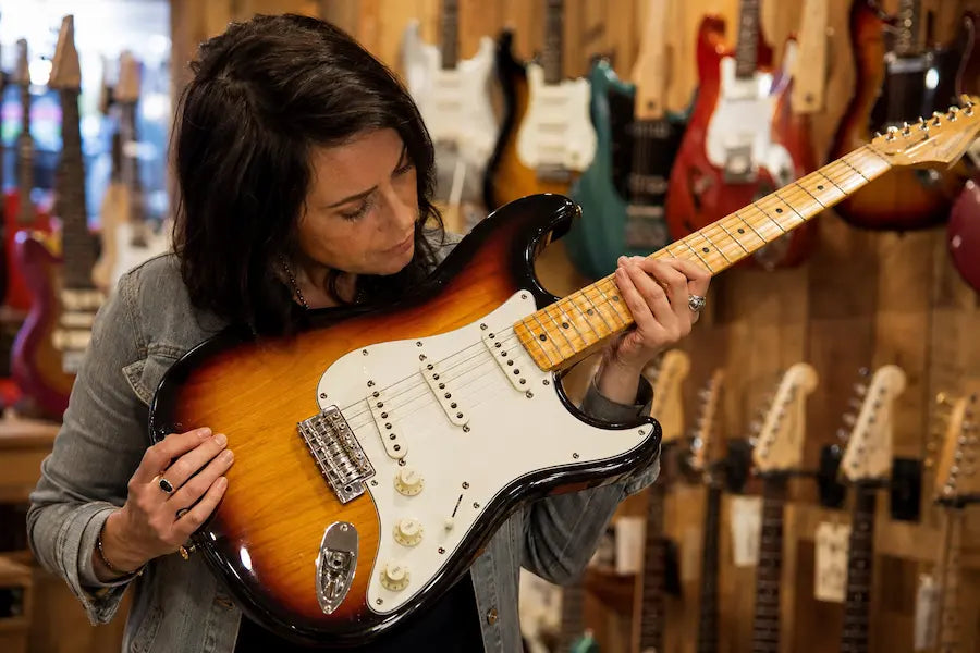 Hands adjusting electric guitar pickups and tuning pegs
