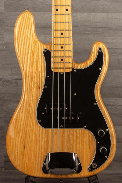 A used Fender Precision Bass from 1976 with a natural finish, visible wood grain, and a black control plate. The instrument is displayed in a vertical orientation with the headstock at the top.