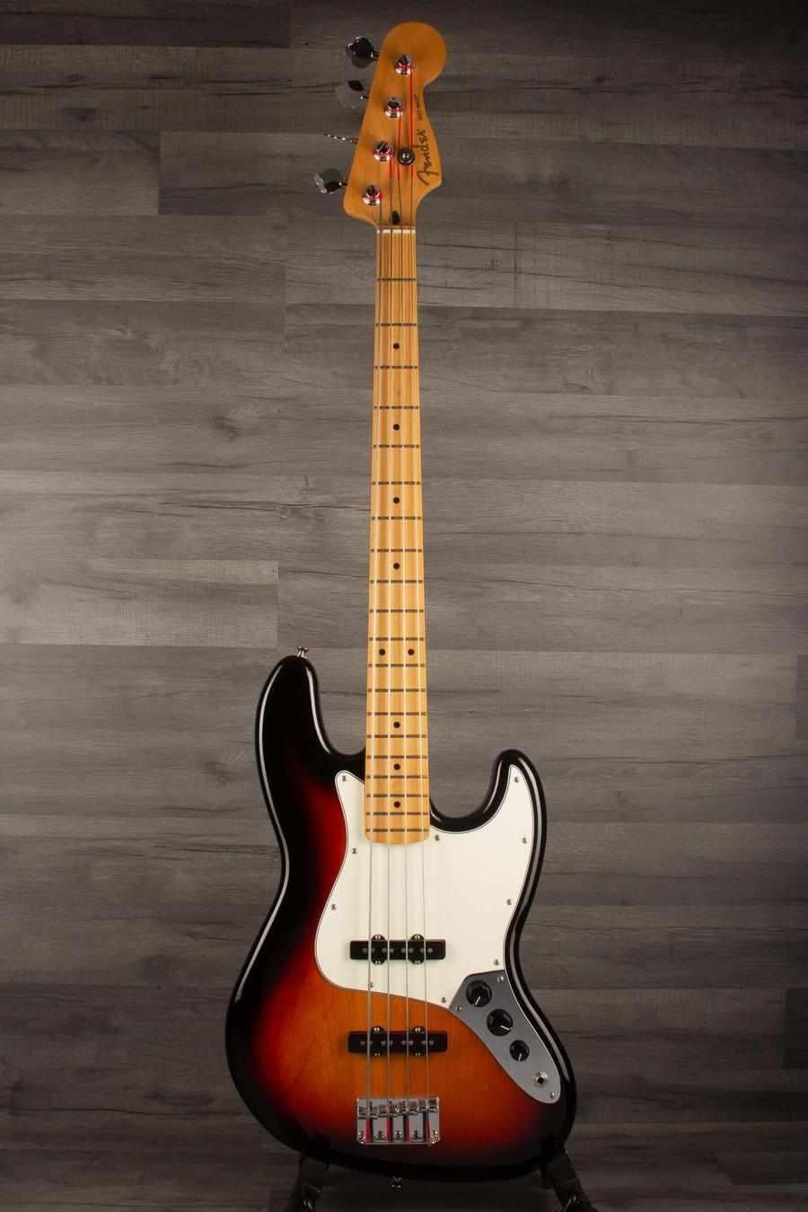 Fender Player Jazz Bass Guitar, Maple neck, 3 tone sunburst on display against a dark wood backdrop.