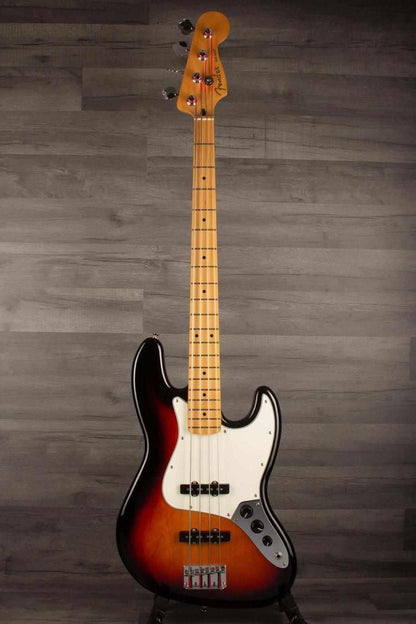 Fender Player Jazz Bass Guitar, Maple neck, 3 tone sunburst on display against a dark wood backdrop.