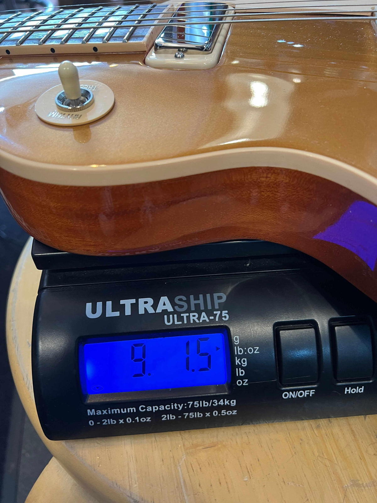 Gibson 2015 Les Paul Deluxe Gold top weighing 9.15 lbs on digital scale with guitar neck visible.