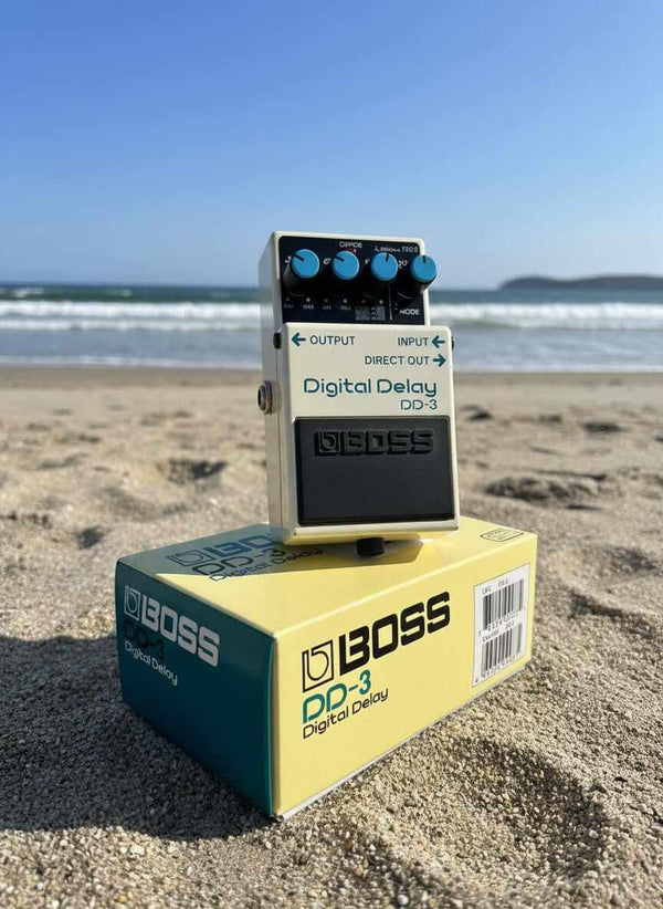 USED Boss Dd-3 digital delay pedal displayed on the beach with waves in the background.