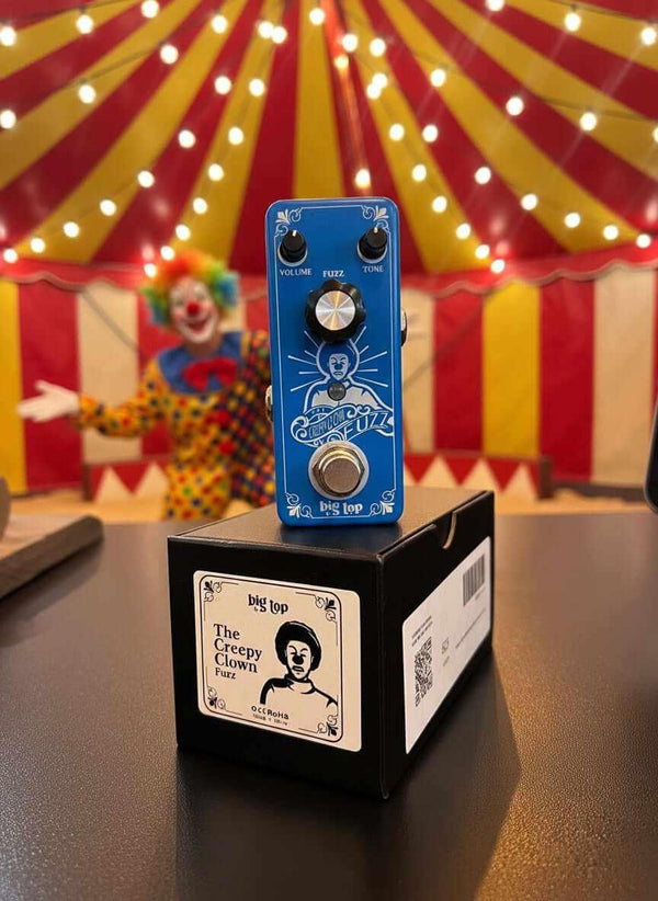 Blue guitar effects pedal on a black box with a clown and circus tent in the background