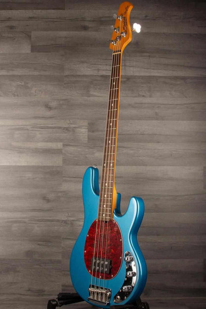 USED - Sterling by Music Man Stingray Ray24 Bass Guitar - Toluca Lake Blue on display against a gray wooden backdrop.