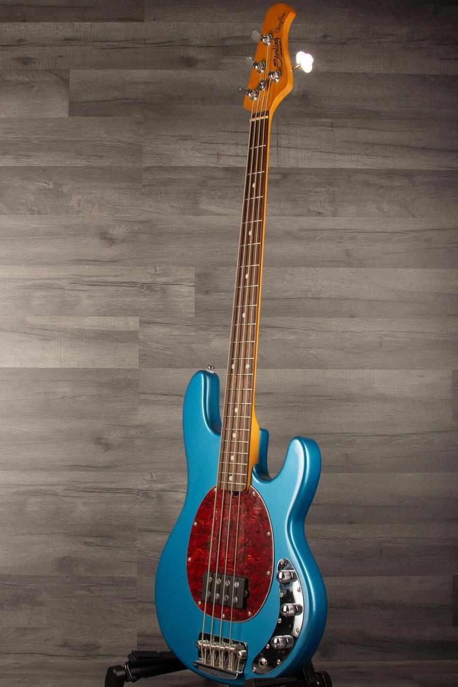 USED - Sterling by Music Man Stingray Ray24 Bass Guitar - Toluca Lake Blue on display against a gray wooden backdrop.