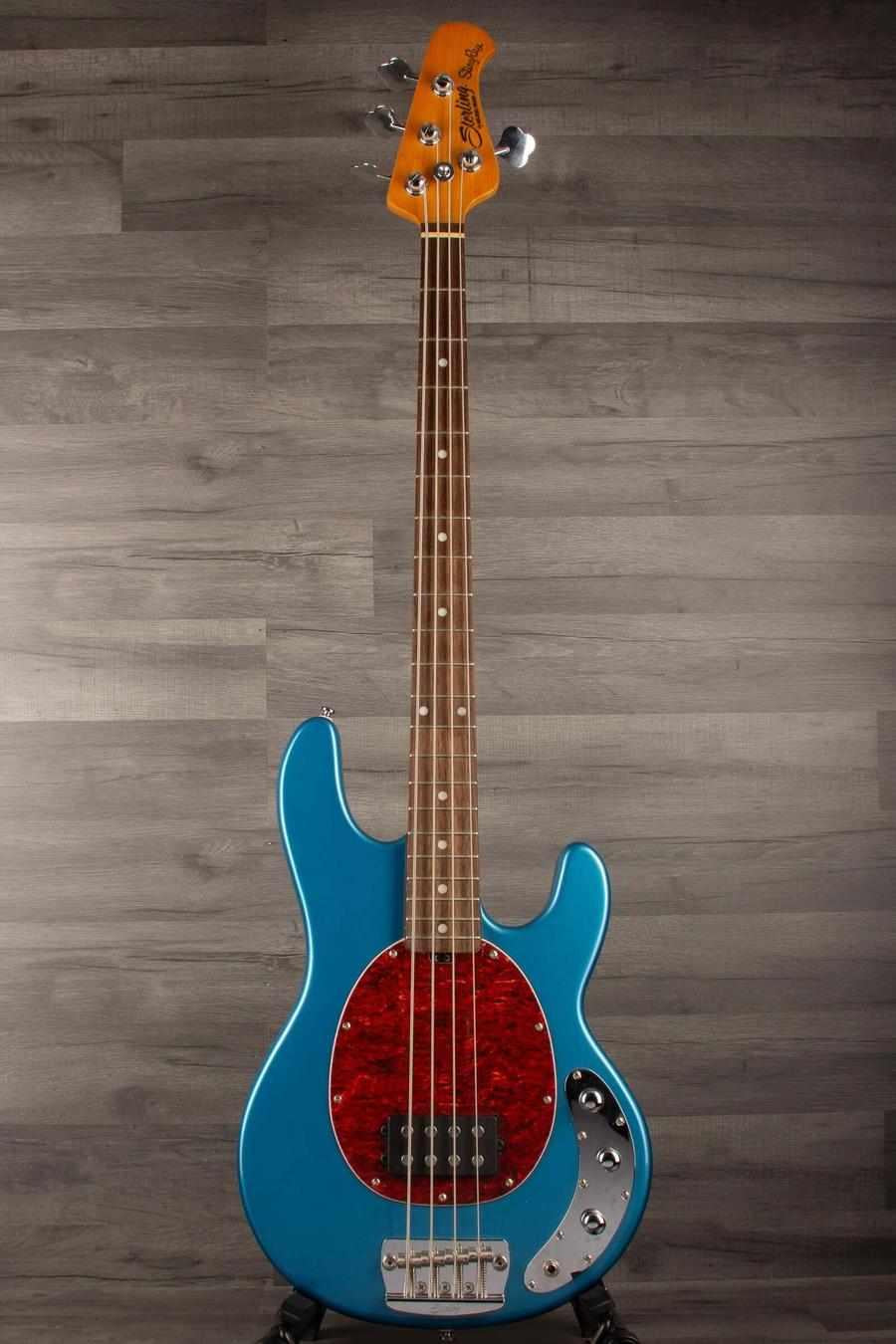 USED - Sterling by Music Man Stingray Ray24 Bass Guitar - Toluca Lake Blue on display against a wooden backdrop.