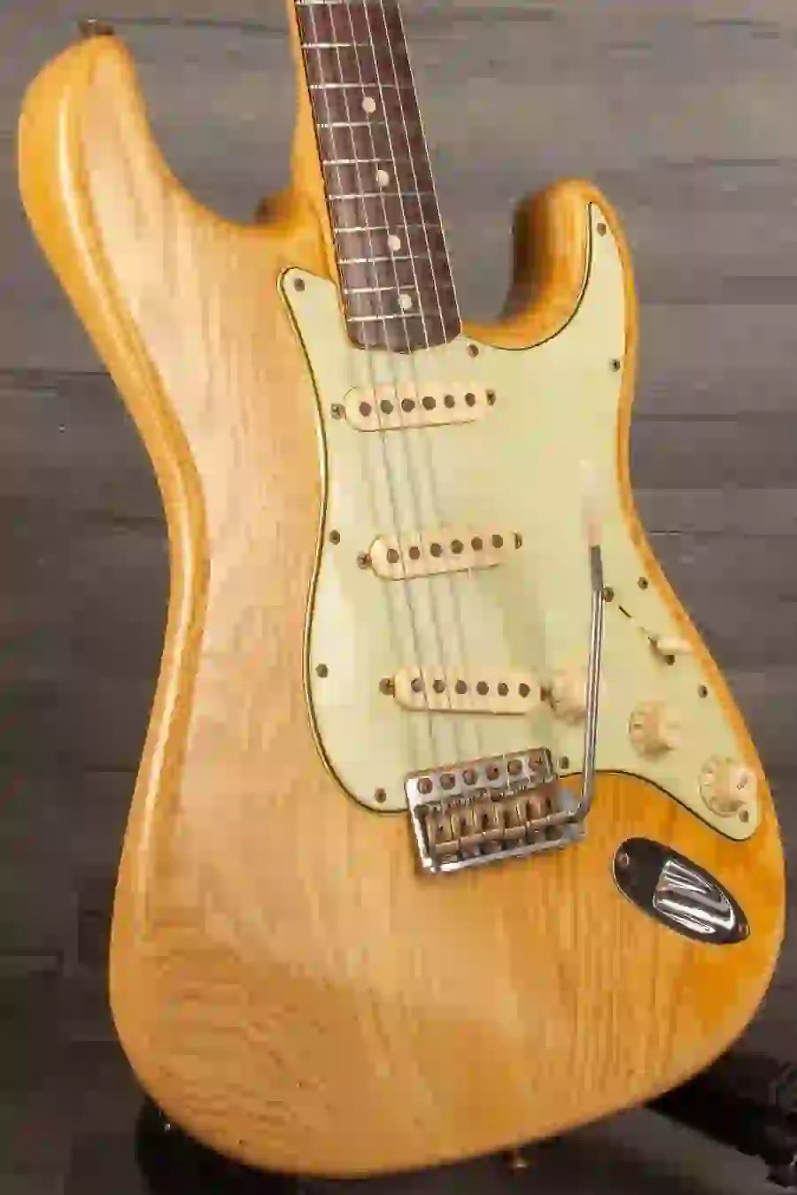 Close-up of a vintage electric guitar with a natural wood finish and white pickguard.