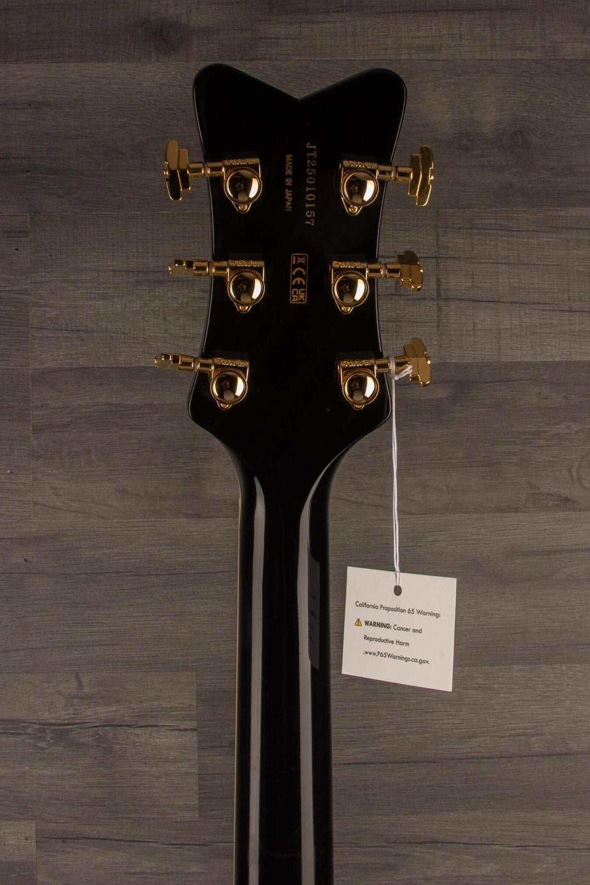 Back view of G6134TG Limited Edition Paisley Penguin™ guitar headstock with gold tuners on a dark surface.